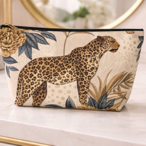Leopard floral accessory pouch with gold botanical design sitting on a marble table in an elegant neutral setting.