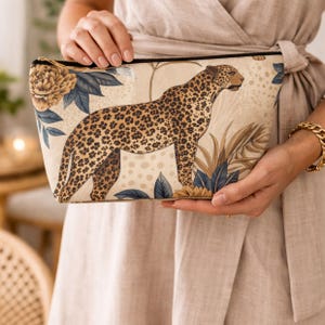 Woman holding leopard floral zipper pouch with neutral gold design, styled as a chic accessory and travel bag.