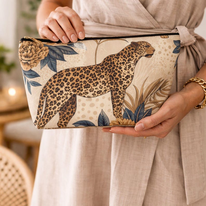 Woman holding leopard floral zipper pouch with neutral gold design, styled as a chic accessory and travel bag.