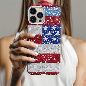 May include: A phone case featuring a design of the American flag. The case has a red, white, and blue color scheme with a speckled texture. The stars and stripes are clearly visible, creating a patriotic theme.