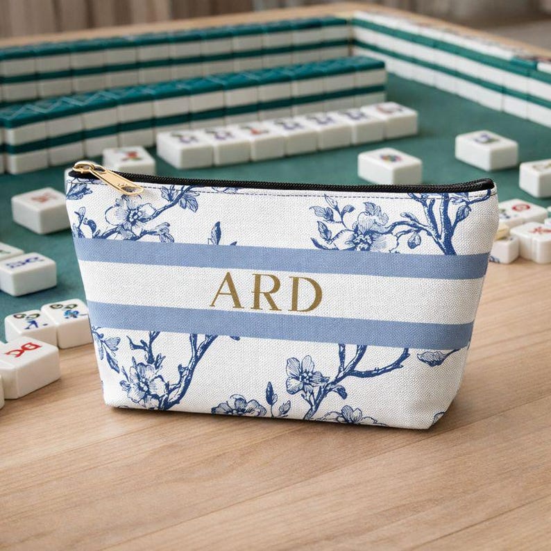 Custom initials Mahjong accessory bag displayed on a wooden table with a Mahjong game and tiles in the background.