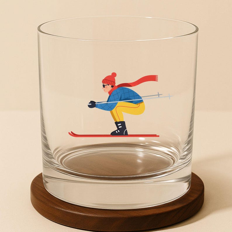 Whimsical après ski whiskey glass with a skier in a classic downhill pose wearing a red scarf and hat.