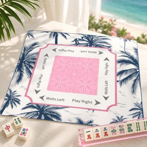 Pink coastal Mahjong mat with palm tree design on a light wood table, styled in a Palm Beach setting with ocean view, Mahjong tiles, and acrylic rack for a preppy beach house aesthetic.