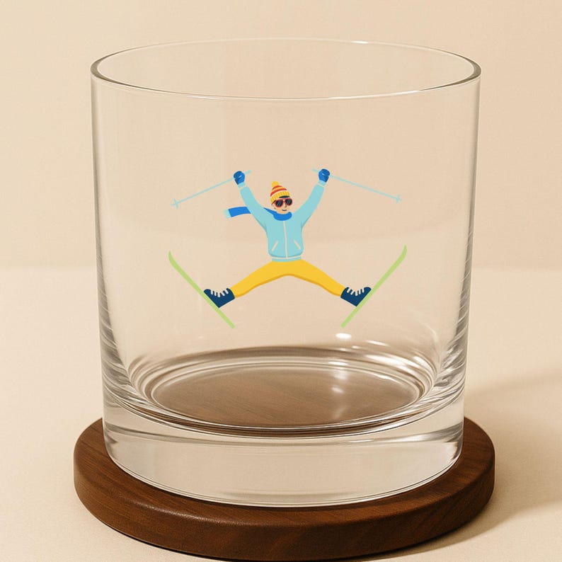 Cute ski whiskey glass showing a whimsical skier mid-jump in a teal jacket and colorful scarf.