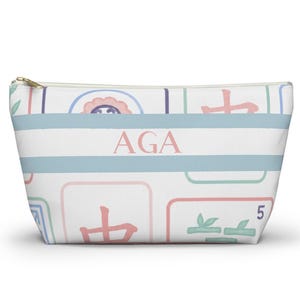 Personalized Mahjong accessory pouch with a pastel Mahjong tile pattern in soft pink, blue, mint, and lavender. The pouch features a gold zipper closure and a blue-and-white striped center panel with pink monogram initials.
