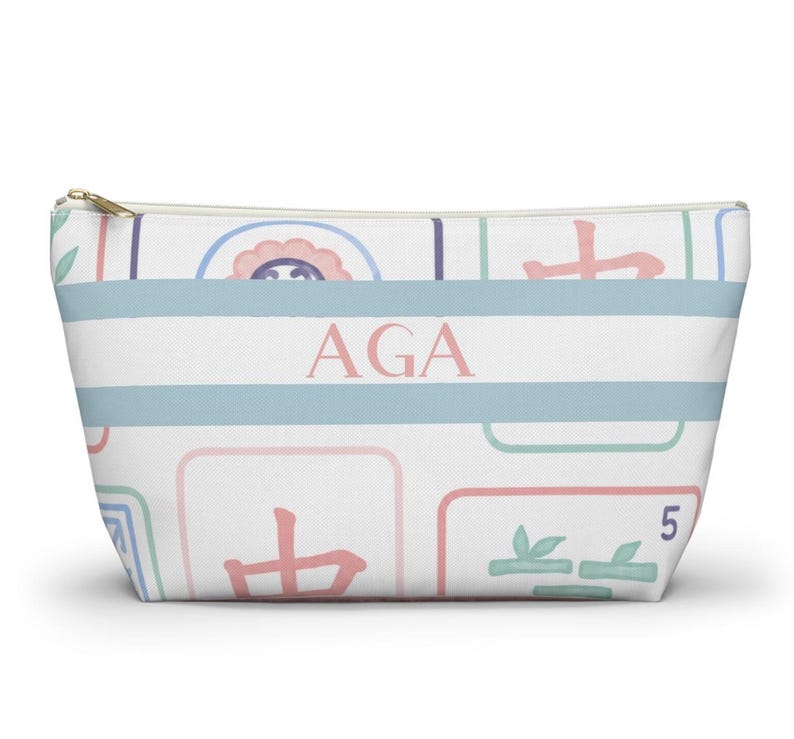 Personalized Mahjong accessory pouch with a pastel Mahjong tile pattern in soft pink, blue, mint, and lavender. The pouch features a gold zipper closure and a blue-and-white striped center panel with pink monogram initials.