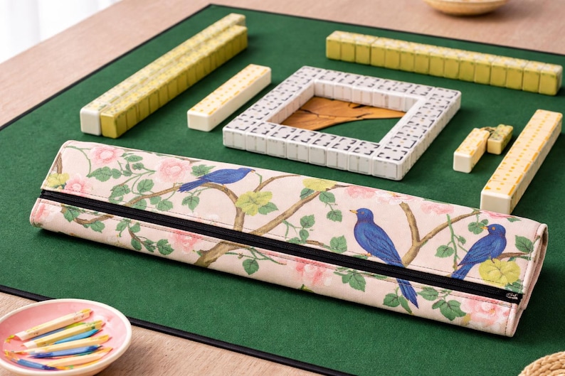Toile Mahjong tile rack wrapper with blue birds and pink floral design placed on green Mahjong table mat with tiles arranged around it.