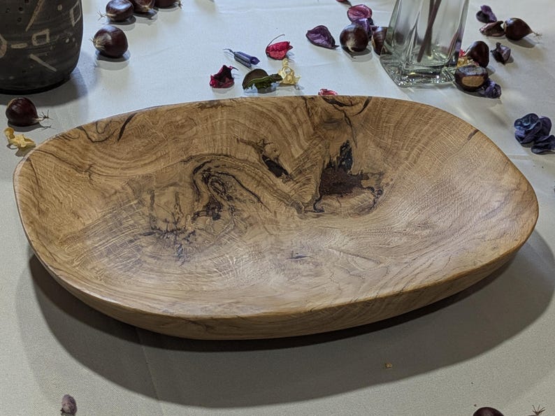 Un plateau en bois de forme ovale avec un motif de grain de bois naturel. Le plateau est brun clair avec des accents brun foncé et une finition lisse et polie. Il est vide et repose sur une surface de couleur claire.