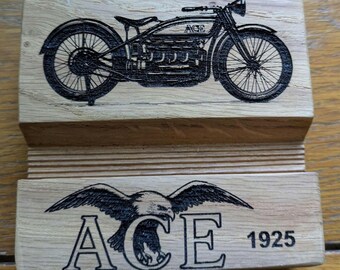 May include: Wooden phone stand featuring a detailed black illustration of an "ACE" motorcycle. The stand also displays an eagle graphic with the word "ACE" and the year "1925". The stand is made of light-colored wood.