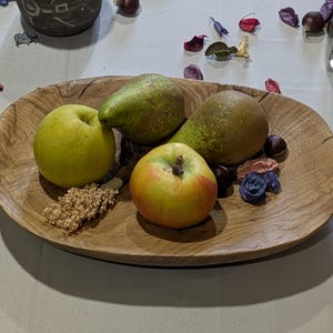 Un plateau ovale en bois rempli de fruits frais. Le plateau contient deux poires vertes, deux pommes et des éléments décoratifs. Les pommes sont jaunes et rouges, et les poires sont vertes. Le plateau est posé sur une surface claire.