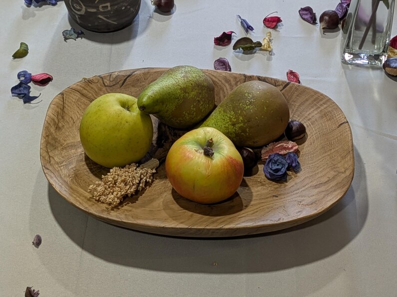 Un plateau ovale en bois rempli de fruits frais. Le plateau contient deux poires vertes, deux pommes et des éléments décoratifs. Les pommes sont jaunes et rouges, et les poires sont vertes. Le plateau est posé sur une surface claire.
