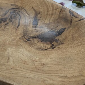 Un plateau en bois fait à la main avec une finition marron clair naturelle. Le plateau présente des motifs de grain de bois brun foncé et une forme rectangulaire. La texture du bois est visible, mettant en valeur les nœuds et les tourbillons naturels. Ce plateau décoratif est idéal pour servir ou exposer.