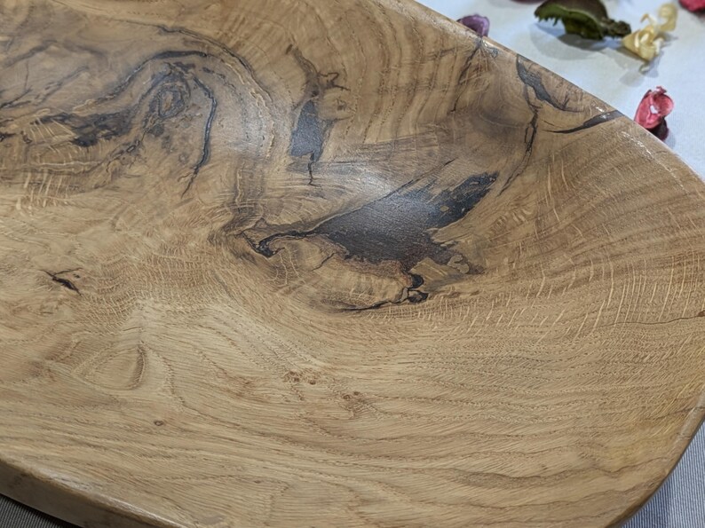 Un plateau en bois fait à la main avec une finition marron clair naturelle. Le plateau présente des motifs de grain de bois brun foncé et une forme rectangulaire. La texture du bois est visible, mettant en valeur les nœuds et les tourbillons naturels. Ce plateau décoratif est idéal pour servir ou exposer.