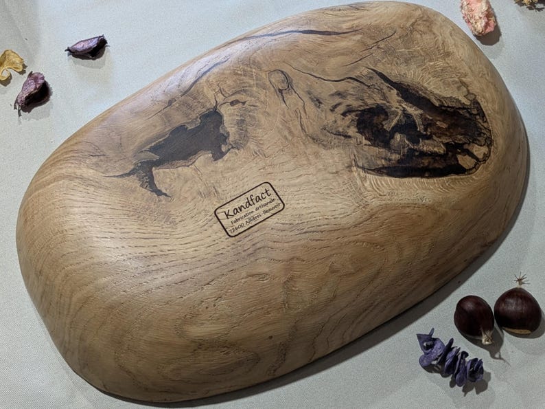 le dessous d'un plateau en bois ovale fait à la main avec une finition naturelle veinée. Le plateau présente des motifs sombres et complexes et une surface lisse et polie. L'étiquette sous le plateau indique "Kandfact". Ce plateau décoratif est parfait pour servir ou exposer.