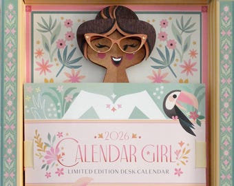 May include: A decorative desk calendar for 2026, featuring a wooden cutout of a woman with glasses. The calendar has a floral and toucan design with the text "CALENDAR GIRL" and "LIMITED EDITION DESK CALENDAR". The calendar is in a decorative box.