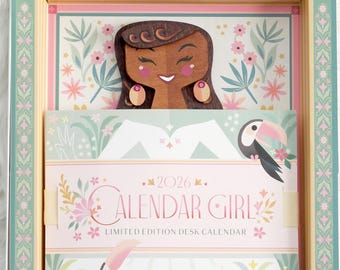 May include: A decorative desk calendar with a wooden cutout of a woman's face and a toucan illustration. The calendar is titled "CALENDAR GIRL" with the year "2026" and floral accents. The design is in a box with a floral and geometric pattern.