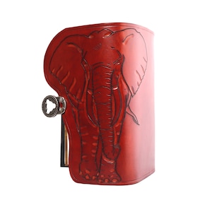 May include: A red leather journal with an embossed elephant design. The journal features a metal clasp and a detailed illustration of an elephant on the front cover. The leather has a rich, textured appearance.