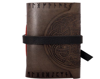 May include: A brown leather journal with a black strap closure. The journal features embossed Celtic knot designs and runes. The pages are red. The journal is closed and ready to be written in.
