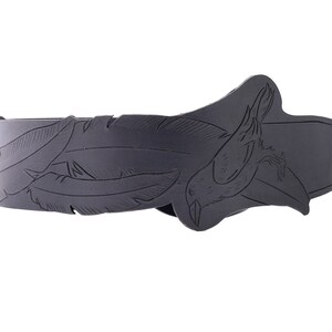 May include: A black leather belt with a decorative feather and bird design. The belt features carved feathers along the strap and a bird motif on the buckle. The belt is a dark gray color and appears to be made of leather.