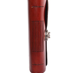 May include: A cylindrical, reddish-brown leather journal with a metal clasp. The journal has vertical stitched lines on the front and a flap closure. The leather has a polished finish, and the journal appears to be new.
