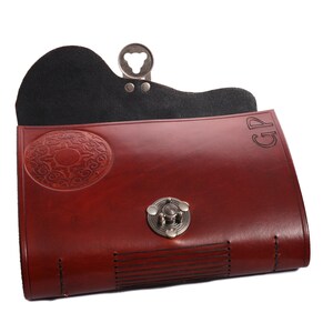 May include: A burgundy leather clutch with a decorative oval design and a silver clasp. The clutch has a black interior and the initials "GP" are visible on the top right corner. The clutch is closed with a silver clasp.
