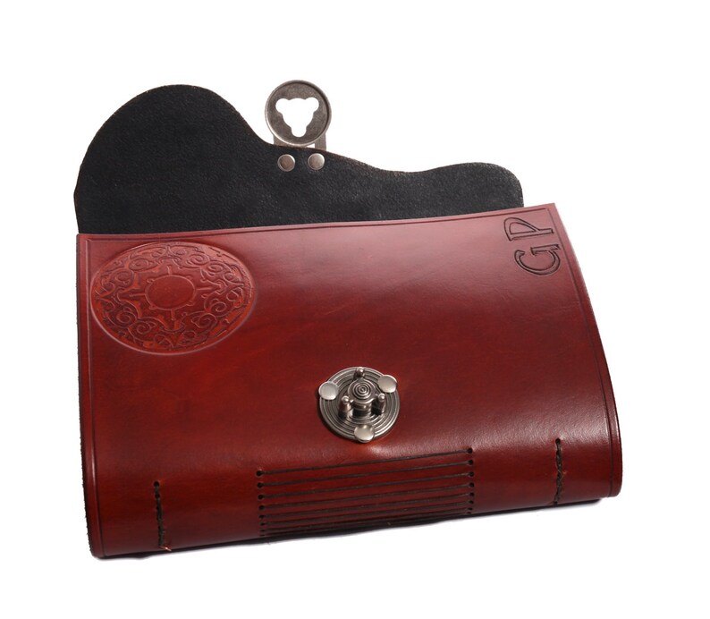 May include: A burgundy leather clutch with a decorative oval design and a silver clasp. The clutch has a black interior and the initials "GP" are visible on the top right corner. The clutch is closed with a silver clasp.