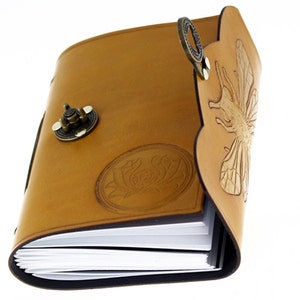 May include: A tan leather journal with a decorative bee and floral design. The journal has a metal clasp and a decorative metal ring. The pages are white and the edges are black.