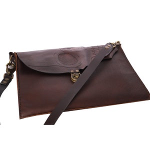Pode incluir: Bolsa mensageiro de couro castanho escuro com um design de caveira em relevo na aba. A bolsa possui uma longa al&ccedil;a de ombro ajust&aacute;vel e um fecho de metal. Feita de couro castanho.