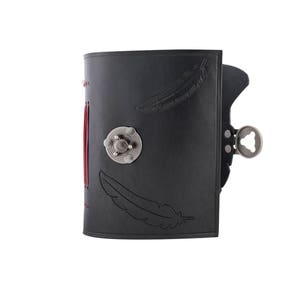 May include: Black leather journal with feather imprints and a silver clasp. The journal has red stitching along the spine and a decorative silver metal closure. The journal is closed.