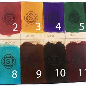 May include: A color chart displaying twelve swatches of dyed leather. The colors include blue, red, yellow, purple, green, black, tan, turquoise, brown, dark brown, bordeaux, and slate grey. Each swatch has a decorative emblem and a number.