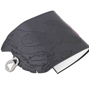 May include: A dark gray journal with a raven design embossed on the cover. The raven is surrounded by feathers. The journal has a silver-colored clasp and a red edge. The pages are white.
