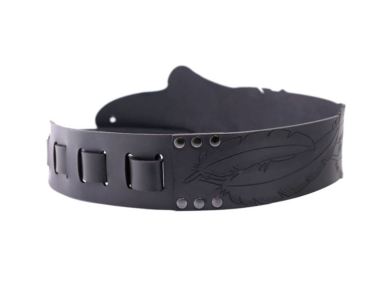 May include: A black leather belt with a decorative feather design. The belt features a series of rectangular loops and is secured with rivets. The design is embossed into the leather, creating a textured appearance. This belt is suitable for various outfits.