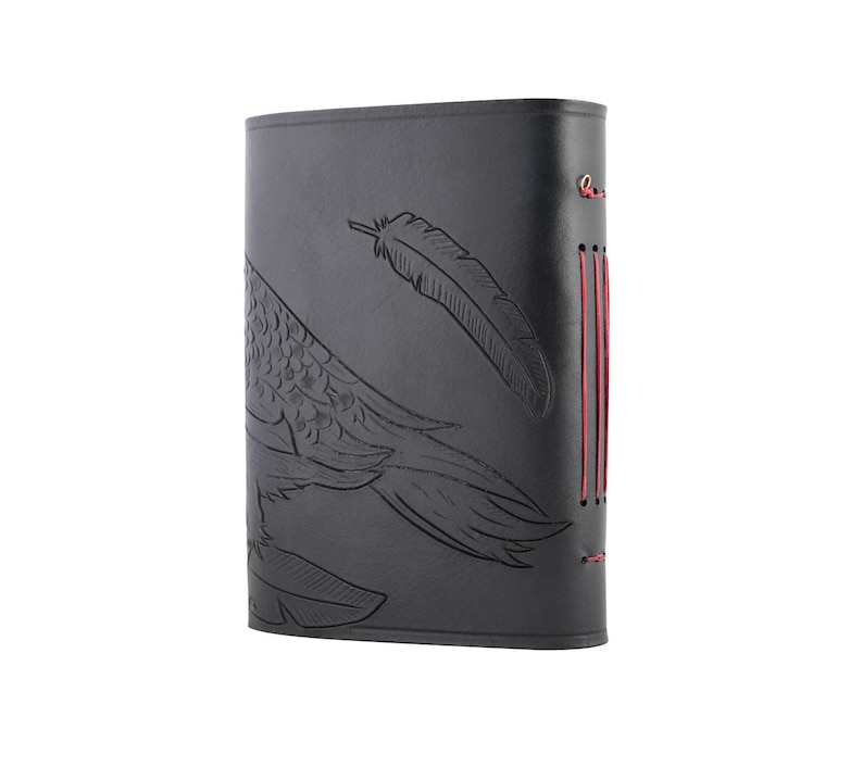 May include: Black leather journal with a debossed feather and bird wing design. The journal has red stitching along the spine. The cover is a solid black color.