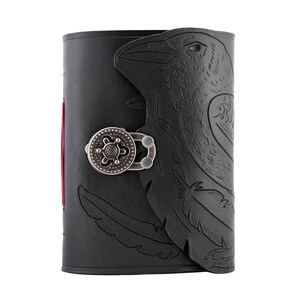 May include: Black leather journal with a raven design embossed on the cover. The journal features a decorative metal clasp and red-edged pages. The raven design includes feathers and the bird's head.