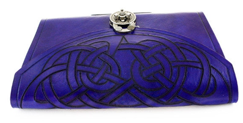 May include: A handcrafted, deep blue leather journal with a Celtic knot design embossed on the cover. The journal features a silver-toned clasp and a detailed, interwoven pattern. The cover is a rich, saturated blue.