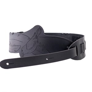 May include: A black guitar strap with a detailed, embossed design featuring a bird. The strap is made of leather and has adjustable slots for length. The design is centered on the shoulder area of the strap.