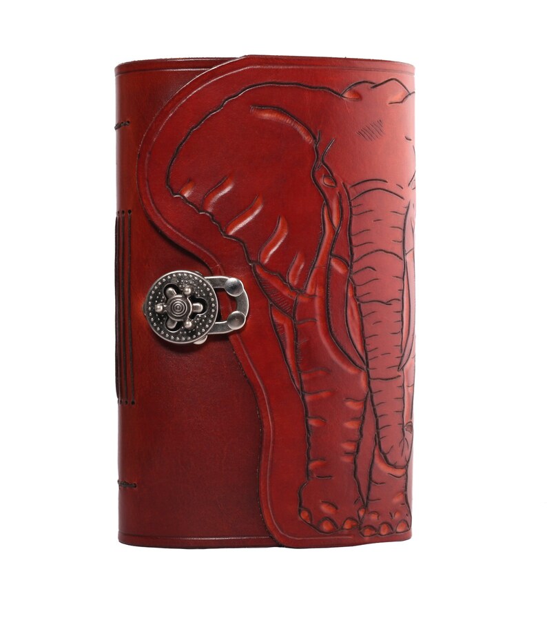 May include: A burgundy leather journal with an embossed elephant design. The journal features a decorative metal clasp and a stitched spine. The elephant is detailed with etched lines, and the leather has a rich, textured appearance.