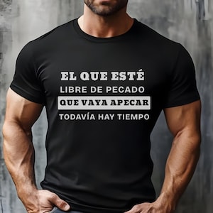 May include: Black t-shirt with white text in Spanish: "El que esté libre de pecado que vaya a pecar, todavía hay tiempo." The shirt has a crew neck and short sleeves.