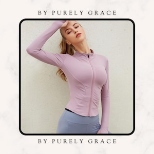May include: A long-sleeved, light purple zip-up top with a mock neck. The top has a fitted silhouette and is made of a stretchy, athletic fabric. The text "BY PURELY GRACE" is displayed at the top and bottom of the image.