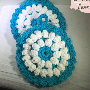 May include: Two crocheted pot holders in a blue and white color scheme. The pot holders are round and have a flower-like design. The pot holders are stacked on top of each other.