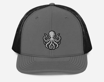 Puede incluir: Una gorra de camionero gris y negra con un diseño de pulpo bordado en blanco.