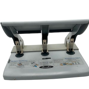 Op de afbeelding: Een grijze Swingline drie-gaats perforator met zwarte accenten. De heavy-duty perforator heeft een maximale capaciteit van 75 vellen. Instructies en het Swingline-logo staan op de basis. Het heeft drie zilveren metalen ponsen.