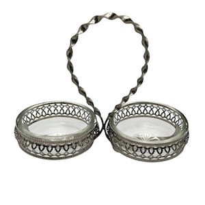 May include: A silver-toned double dish with a twisted handle. Each dish has a clear glass bowl set within a decorative, openwork metal frame. The handle arches above the dishes, connecting them.