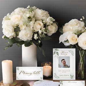 May include: A white memory table with a sign that says "Memory Table". There are white flowers in vases, candles, and cards with the text "Share a memory" and "Please take a card and share a memory of our beloved John Davis".