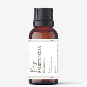 May include: A brown glass bottle with a black cap, labeled "Kimiya FRANKINCENSE Essential Oil". The label also lists the scent as "Woody, Spicy, Balsamic" and the benefits as "Relaxing, Anti-Inflammatory, Spiritual".