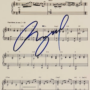 Può includere: Spartito musicale con note e simboli, con una firma blu scritta a mano. La parte superiore della pagina include la parola "Freely" e notazioni musicali. Il testo "Fast three, in one = 58" è anch'esso visibile.