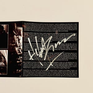 May include: A close-up of a handwritten note signed by a musician. The note is written on a white piece of paper and includes a description of the musician's creative process. The note is surrounded by a black and white image of a building.