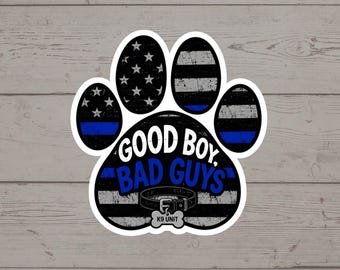 Puede incluir: Una pegatina con forma de huella que presenta un patrón de bandera desgastado en blanco y negro con una fina línea azul. El texto dice GOOD BOY, BAD GUYS. Un gráfico de un collar de perro con una placa en forma de hueso que dice K9 UNIT.