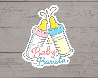 Puede incluir: Una pegatina que muestra dos biberones chocando, uno con tapa rosa y otro con tapa azul, ambos con tetinas amarillas. El texto Baby Barista aparece debajo en letra cursiva rosa y azul, decorado con pequeñas estrellas amarillas y azules.