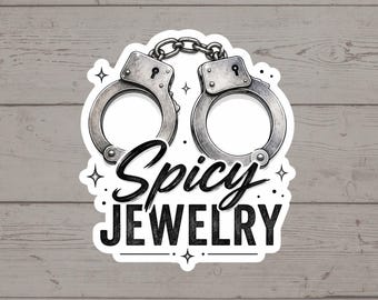 Puede incluir: Una pegatina troquelada con una ilustración en blanco y negro de unas esposas de metal en la parte superior. Debajo de las esposas, el texto dice Spicy JEWELRY en una combinación de letra cursiva y negrita, con pequeños símbolos de estrellas.